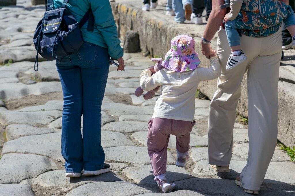 Little girl in pink cap walks in Pompeii held by hand by an adult
