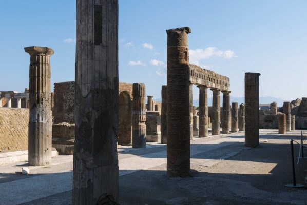 Ruins in the forum of Pompeii with ancient columns under a clear sky.