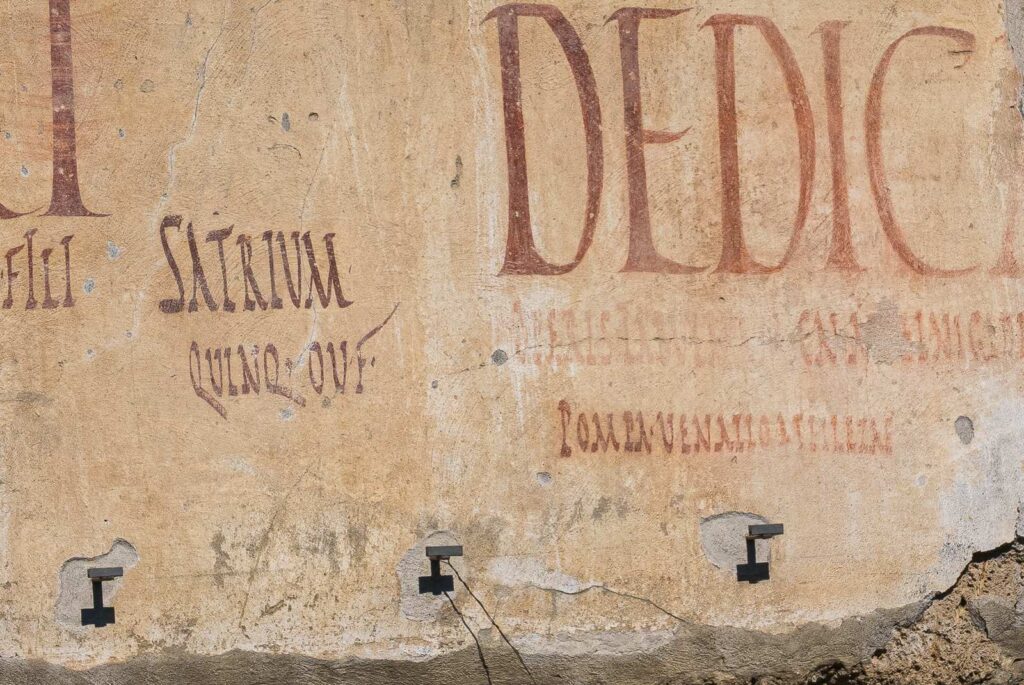 Latin inscription on an ancient wall, with red and black lettering on a beige background.