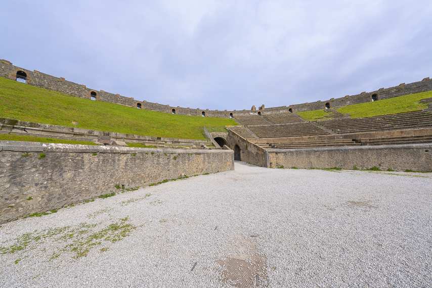 Interior of the Amphitheatre of Pompeii with steps and green lawn.