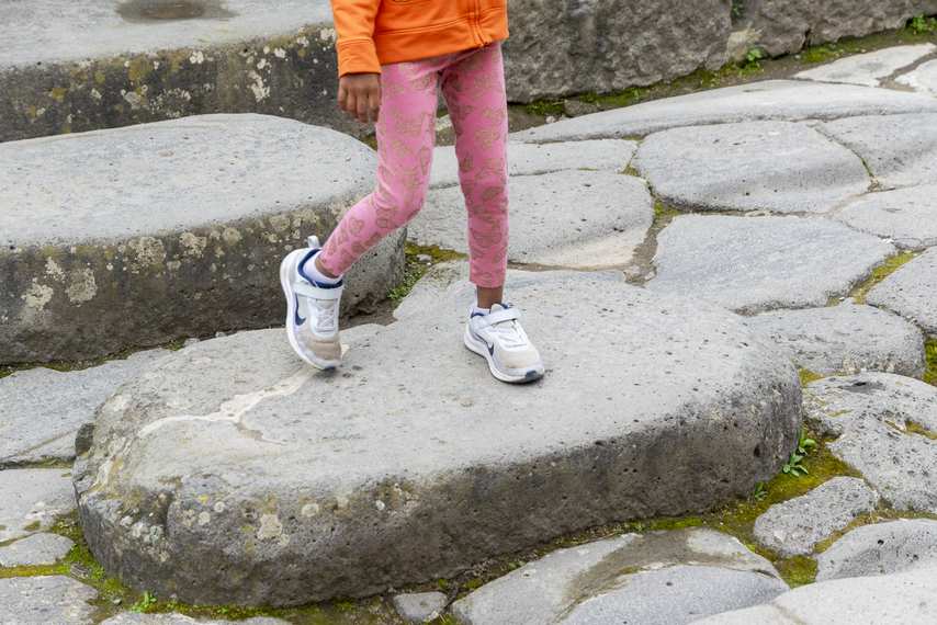 Little girl crossing an ancient Roman road in Pompeii by walking on a raised stone