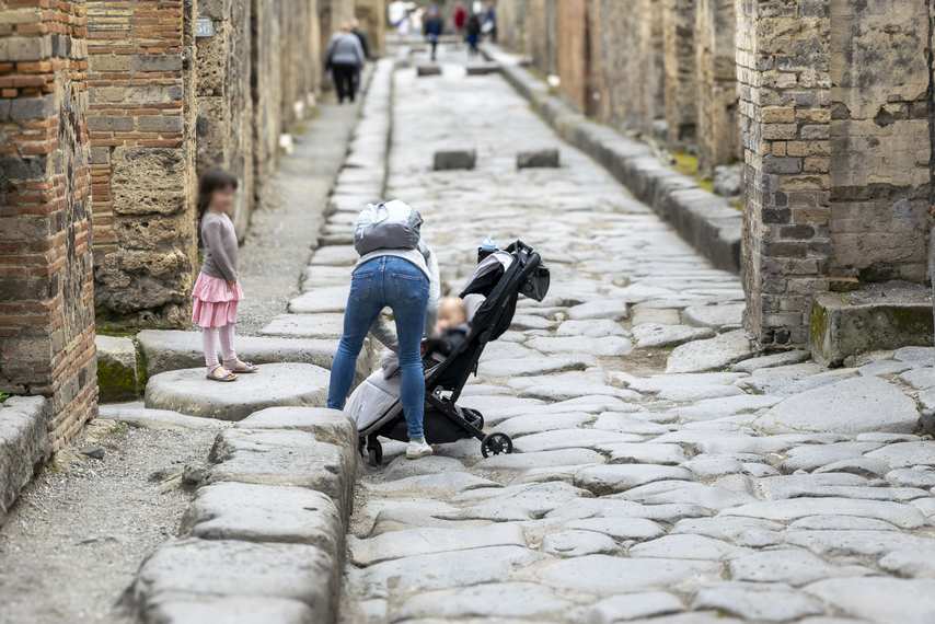 Family with stroller and children among the ancient streets of Pompeii