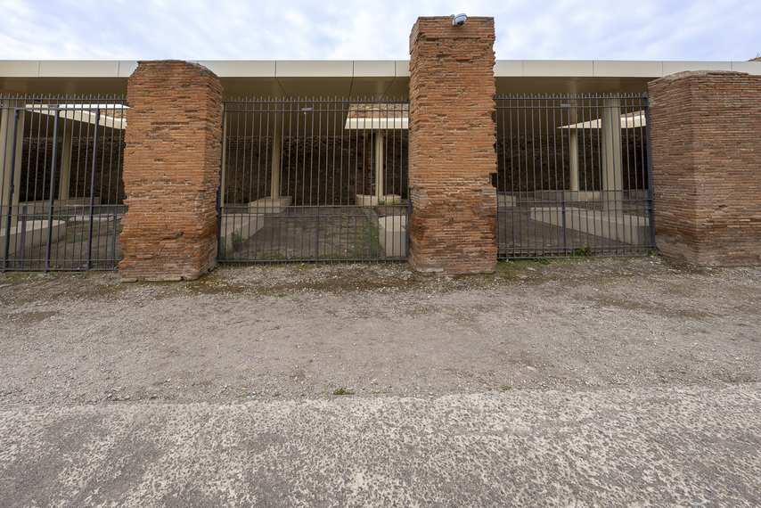 Gated entrance to the Granaries of the Forum at Pompeii, with modern structure and supporting columns