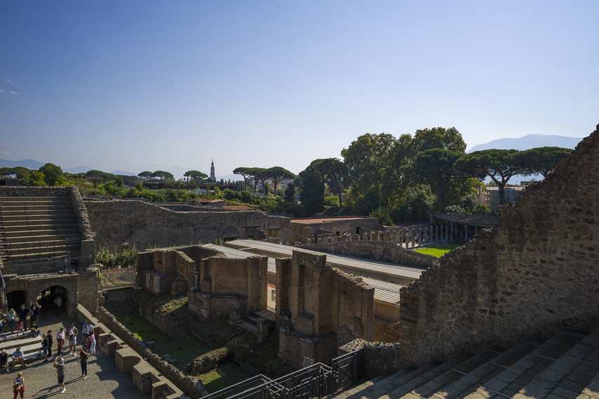 View of the stage and back of the Large Theatre of Pompeii with trees and Quadriporticus in the background